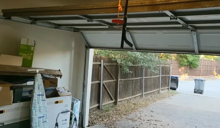 Inside a garage looking out through a raised garage door to the driveway