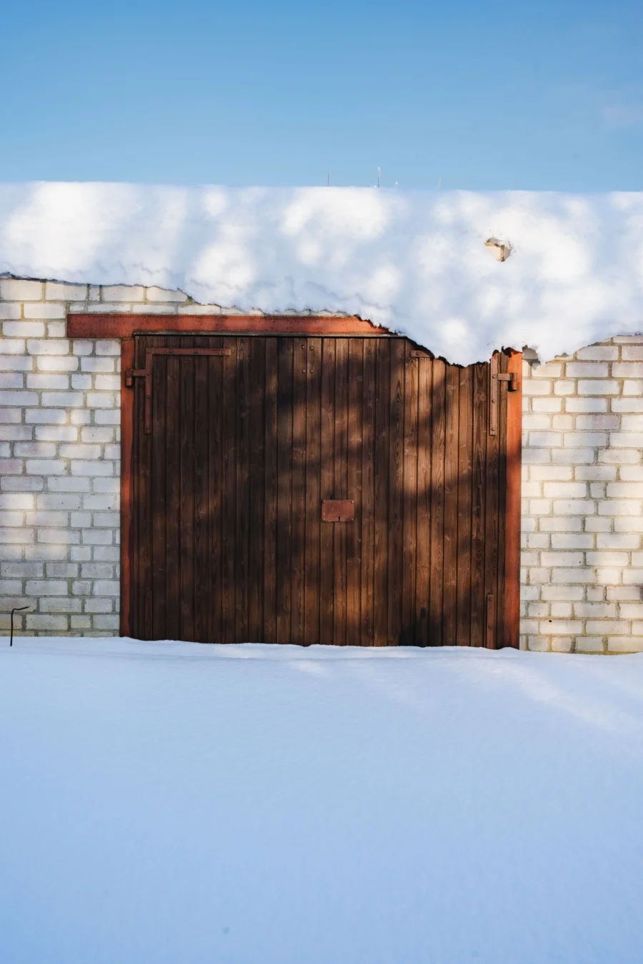 A wooden garage door covered in fresh snow under a clear blue sky